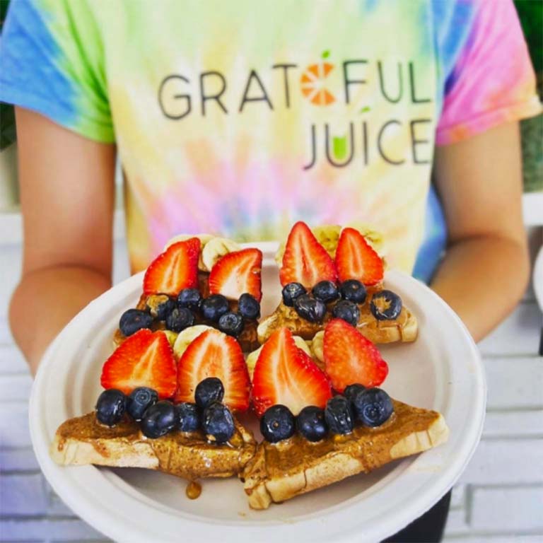 A person holding a plate of toast with peanut butter, strawberries, and blueberries.